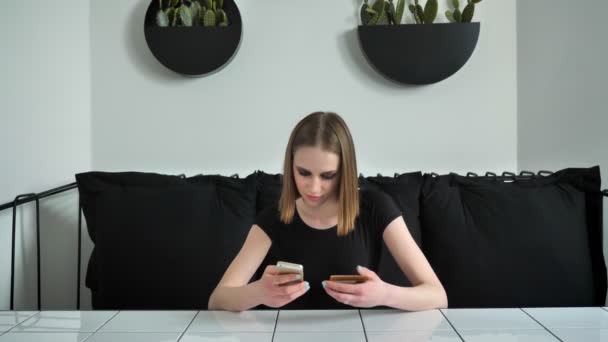 Unga vackra kvinnor med tunga utgör omskrivning på telefon från kort, sitter på soffa, svart och vit café bakgrund — Stockvideo