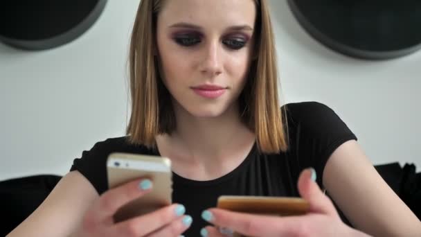 Молоді чарівні жінки з важким макіяжем переписують текст на телефоні з карткового, чорно-білого фону стіни — стокове відео