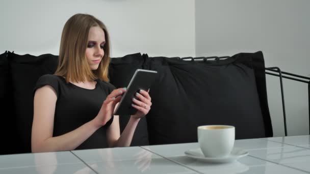 Mladé krásné ženy s těžkými tvoří při používání tabletu a sedí na pohovce, s úsměvem, černé a bílé café pozadí — Stock video