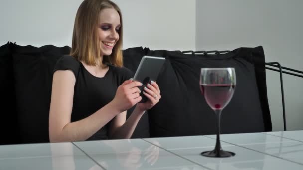 Ağır olan genç çekici kadın tablet kullanma ve kanepe, oturma gülüyor, siyah ve beyaz Cafe arka plan makyaj — Stok video