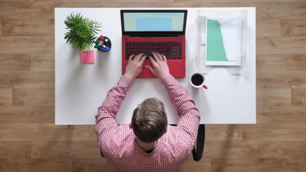 Ung man i glasögon arbetar på laptop, kvinnor att ge honom dokument, topshot, sitter bakom skrivbord — Stockvideo
