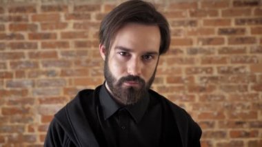 Sakallı genç çekici adam bakar ve gülümser, flört anlayışı, tuğla arka plan