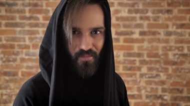 Başlıklı sakallı genç deli adam izliyor kamera, duygusal kavramı, tuğla arka plan