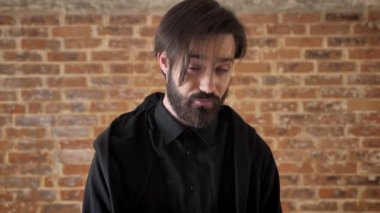 Kameraya, tuğla arka plan izlerken kaş, Genç kayıtsız adam yükseltir