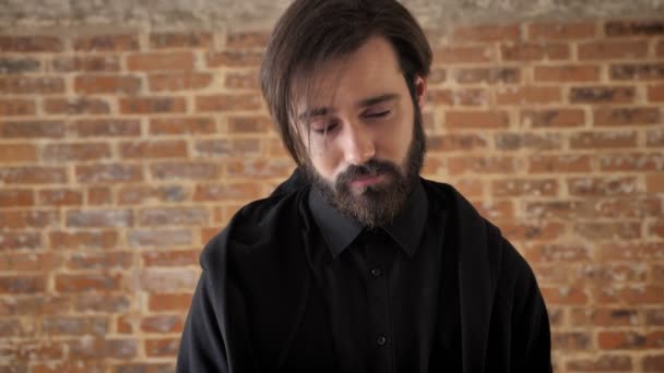 Young atractive man with beard is acting, watching at camera, flirt conception, brick background