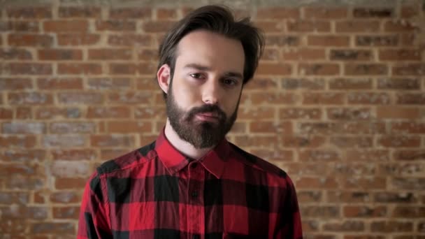 Jonge aantrekkelijke man met baard is kijken op camera, baksteen achtergrond — Stockvideo