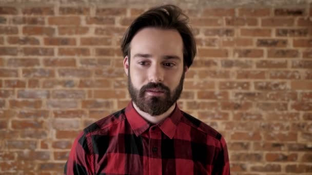 Young handsome happy man with beard is thinking, brick background — Stock Video