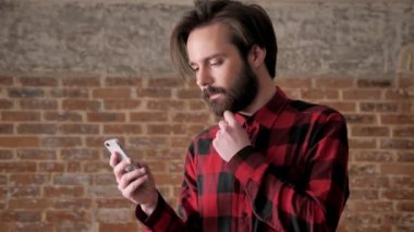 Sakal saatler, genç yakışıklı adamla yakınlaştırır fotoğraflar onun smartphone, comunication kavramı, tuğla arka plan