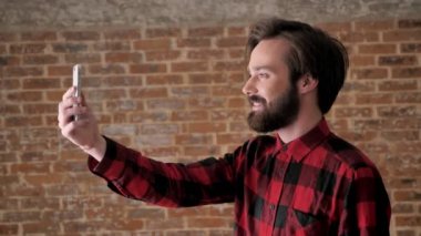 Sakallı genç çekici adam video sohbet içinde smartphone online, comunication kavramı, tuğla arka plan üzerinde konuşuyor.