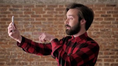 Sakallı genç çekici adam video sohbet içinde smartphone, puan konuşuyor, onaylar, işareti, comunication kavramı, tuğla arka plan gibi