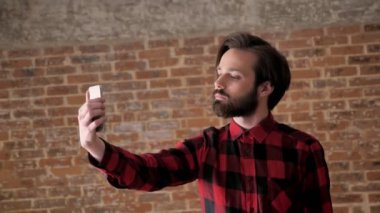 Sakallı genç yakışıklı adam selfie onun smartphone, comunication kavramı, tuğla arka plan yapmak