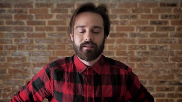 Young cheerful man with beard is scratching your head, thinking process, brick background — Stock Video