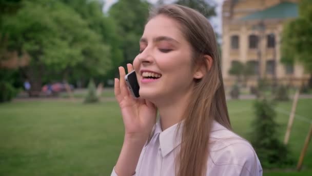 Giovane ragazza carina sta parlando al telefono nel parco in estate, ridendo, concetto di comunicazione — Video Stock