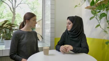 İki genç güzel kadının kafe, bir tanesi oturan bir şey başka bir kadın için söylüyorum hijab Müslüman kadın