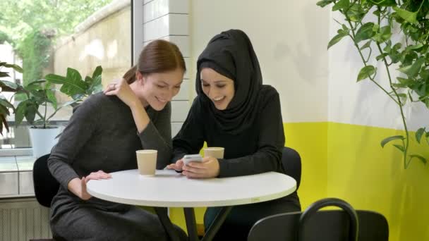 그들 중 하나는 카페에 앉아 두 젊은 아름 다운 여 대 무슬림 여성 hijab에 전화 보고 하 고 웃 고, 행복 — 비디오