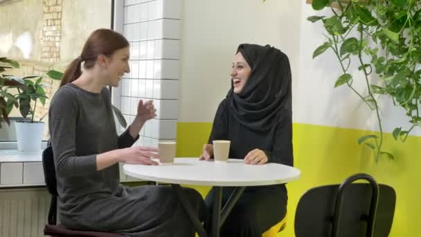 두 젊은 아름 다운 여 대 카페에 앉아서 웃 고, 한 명은 무슬림 여성 hijab, 행복에 — 비디오