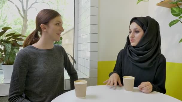 젊은 아름 다운 무슬림 여성 hijab 웃 고, 카페에 앉아 다른 여자에 게 뭔가 말하고 있는 — 비디오