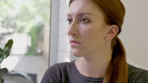 Портрет молодой женщины с хвостиком, сидящей в кафе и смотрящей в камеру, серьезный и решительный — стоковое видео