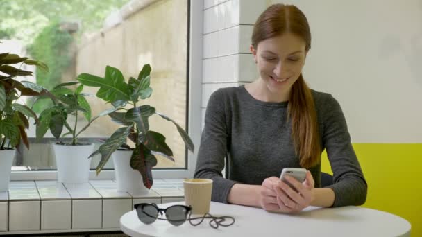 Okouzlující dívka s culíkem, posezení v kavárně a psaní na telefonu, překvapil a usmívá se — Stock video