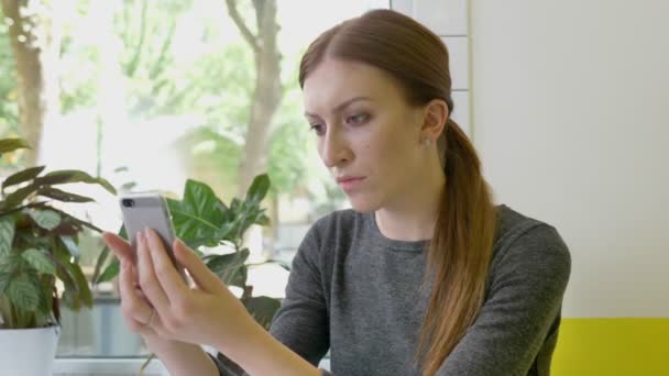 Jonge mooie vrouw met een paardenstaart zitten in Cafe, holding van mobiele en kijken naar telefoon, serieuze en betrokken — Stockvideo