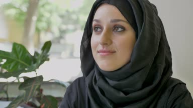 Portre seyir ileri ve ardından kamera, genç güzel Müslüman kadının kafede oturan hijab gülümseyen