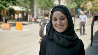 Gülümseyen genç güzel Müslüman kadın kentsel Caddesi üzerinde duran ve kamera, seyir hijab portresi