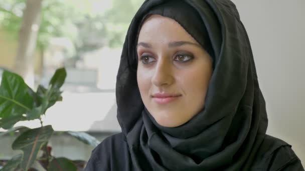 Portrait de jeune jolie femme musulmane en hijab assise dans un café, regardant vers l'avenir, pensant — Video