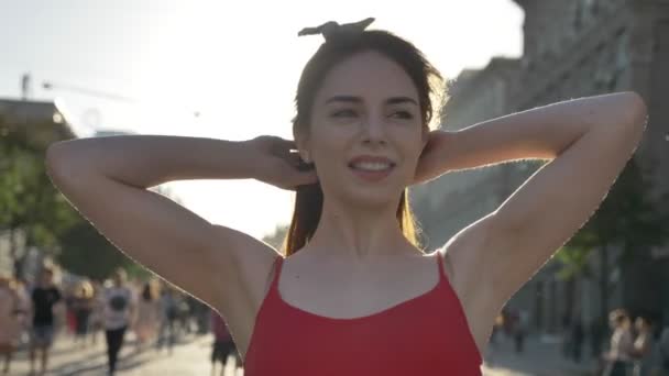 Porträtt av ung vacker kvinna med ingefära hår stående på gatan, lyfta huvudet, röra håret och ler, människor gå runt — Stockvideo