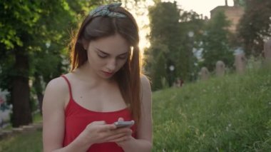 Kızıl saçlarını manifatura telefon ve Park, çimlerin üzerine oturmuş olan büyüleyici kadın gülümseyerek