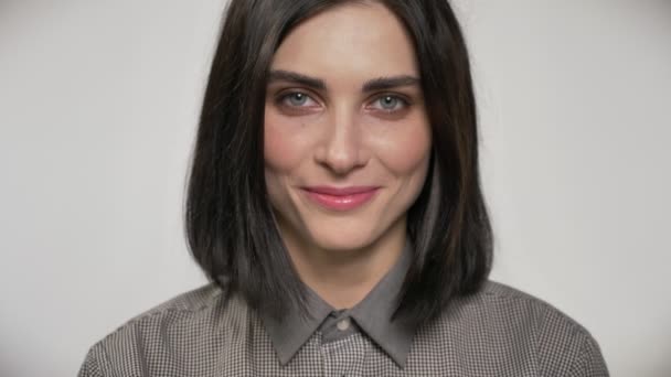 Portrait of young beautiful woman with short brown hair looking straight into camera and laughing, white background — Stock Video