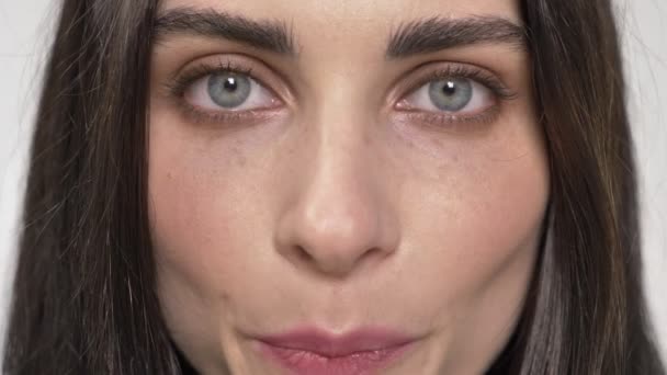 Retrato de una joven mujer bonita con ojos azules mirando directamente a la cámara y parpadeando, ojos cerrados, fondo blanco — Vídeo de stock