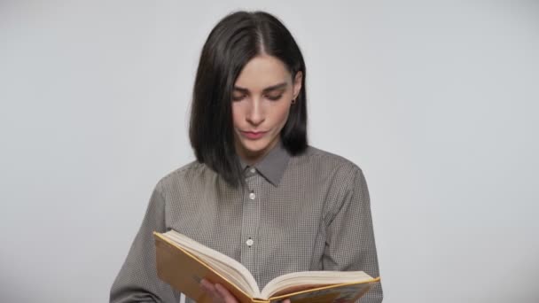 Young beautiful woman with short brown hair holding and reading book, concentrated, white background — Stock Video