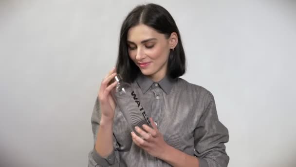 Jonge mooie vrouw met kort bruin haar bedrijf fles met water en aanwijsapparaat fles in de camera, lachend, blij, witte achtergrond — Stockvideo