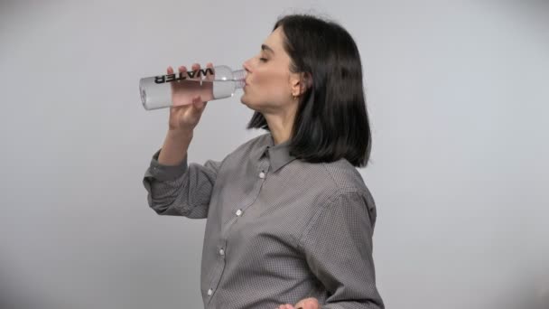 Junge schöne Frau mit kurzen braunen Haaren trinkt aus Flasche mit Wasser, weißer Hintergrund — Stockvideo