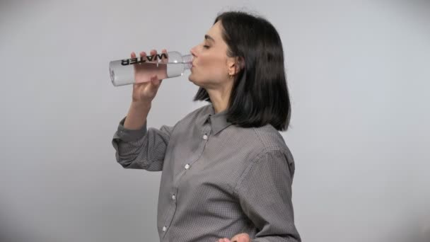 Joven hermosa mujer con pelo castaño corto bebiendo de la botella con agua, fondo blanco — Vídeos de Stock