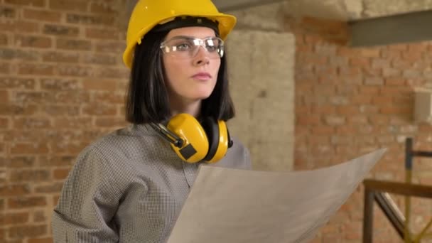 Молодая очаровательная архитектор женщина держит бумагу и глядя вперед, концентрированный, кирпичный фон здания — стоковое видео