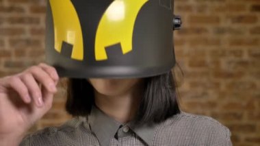 Genç kameraya bakarak kısa kahverengi saçlı kaldırma onu kask, kadın Oluşturucusu, tuğla arka plan güzel kadınlar