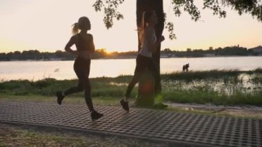 Parkta yakın nehir, köprü üzerinden günbatımı, kilo verme sırasında fitness modelleri koşu, güzel görünüm çalışan iki genç güzel bayanlar
