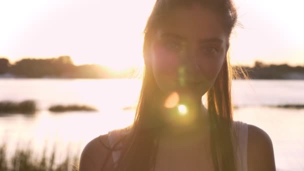 Retrato de una joven hermosa mujer mirando en cámara y sonriendo, destello de lente, río y fondo de la naturaleza — Vídeo de stock