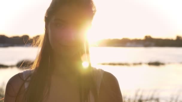 Portrait of young charming woman looking in camera and laughing, sunset and lens flare, river and nature background — Stok Video