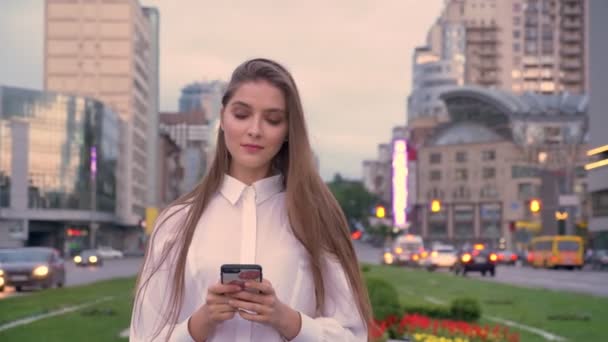 美しい少女にメッセージを入力スマート フォンで夕暮れ時市内中心部に夏、通信の概念 — ストック動画