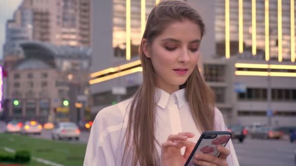 Молодая красивая девушка наблюдает на своем смартфоне на закате в центре города летом, концепция мышления, коммуникационная концепция — стоковое видео