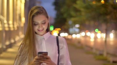 Genç ve çekici bir kız yazın akşam akıllı telefonuna mesaj yazıyor. Gülümsüyor, iletişim kuruyor.