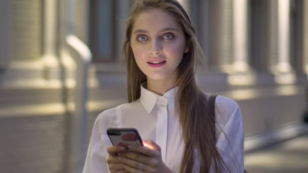 Menina atraente jovem está digitando mensagem em seu smartphone à noite no verão, assistindo a câmera, rindo, conceito de comunicação — Vídeo de Stock