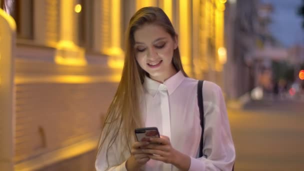 Menina atraente jovem está digitando mensagem em seu smartphone à noite no verão, conceito de pensamento, conceito de comunicação — Vídeo de Stock