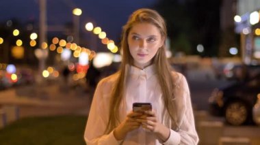 Genç çekici kız ileti onun Smartphone'da akşam şehir merkezinde yazmakta olduğunu yaz, düşünme kavramı, iletişim kavramı