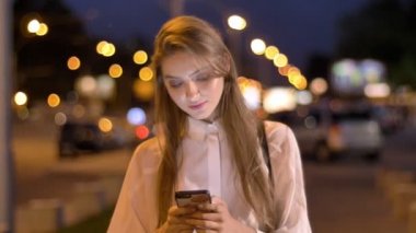 Genç çekici kız ileti onun Smartphone'da akşam şehir merkezinde yaz aylarında, gülümseyen, düşünme kavramı, iletişim kavramı yazmakta olduğunu