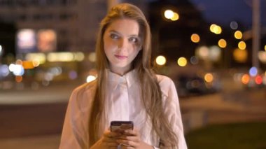 Genç güzel rüya kız ileti onun Smartphone'da akşam şehir merkezinde yazmakta olduğunu yaz, düşünme kavramı, iletişim kavramı