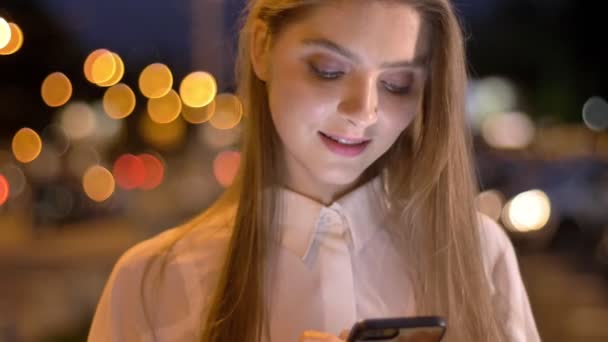 Joven hermosa chica está escribiendo mensaje en su teléfono inteligente en la noche en verano, concepto de ensueño, concepto de comunicación — Vídeos de Stock
