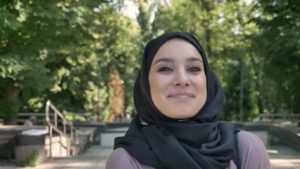 Joven chica musulmana feliz está caminando en el parque durante el día en verano, sonriendo, mirando alrededor, concepto religioso — Vídeos de Stock